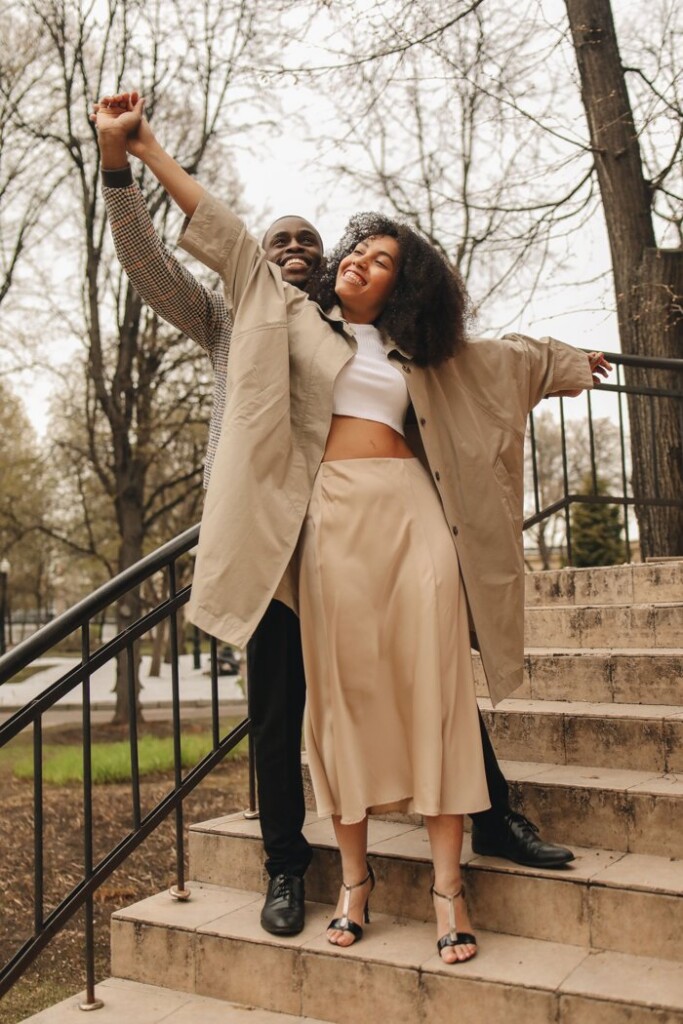 Smiling couple dancing together on park steps, arms outstretched