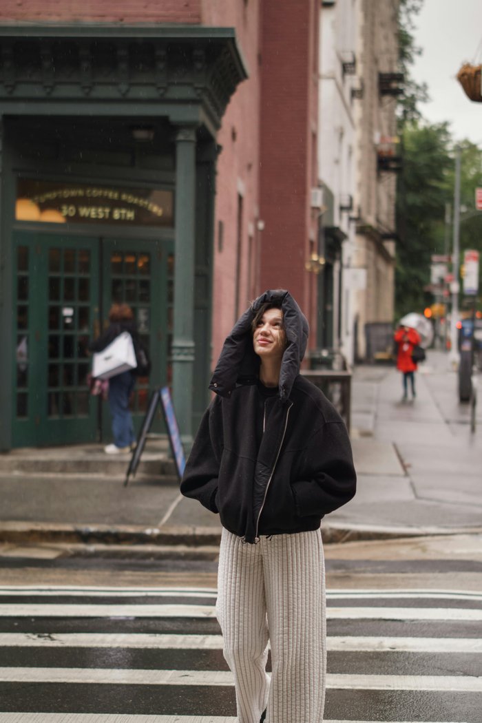Person in a hooded jacket pausing on a rainy city street, looking up at the sky