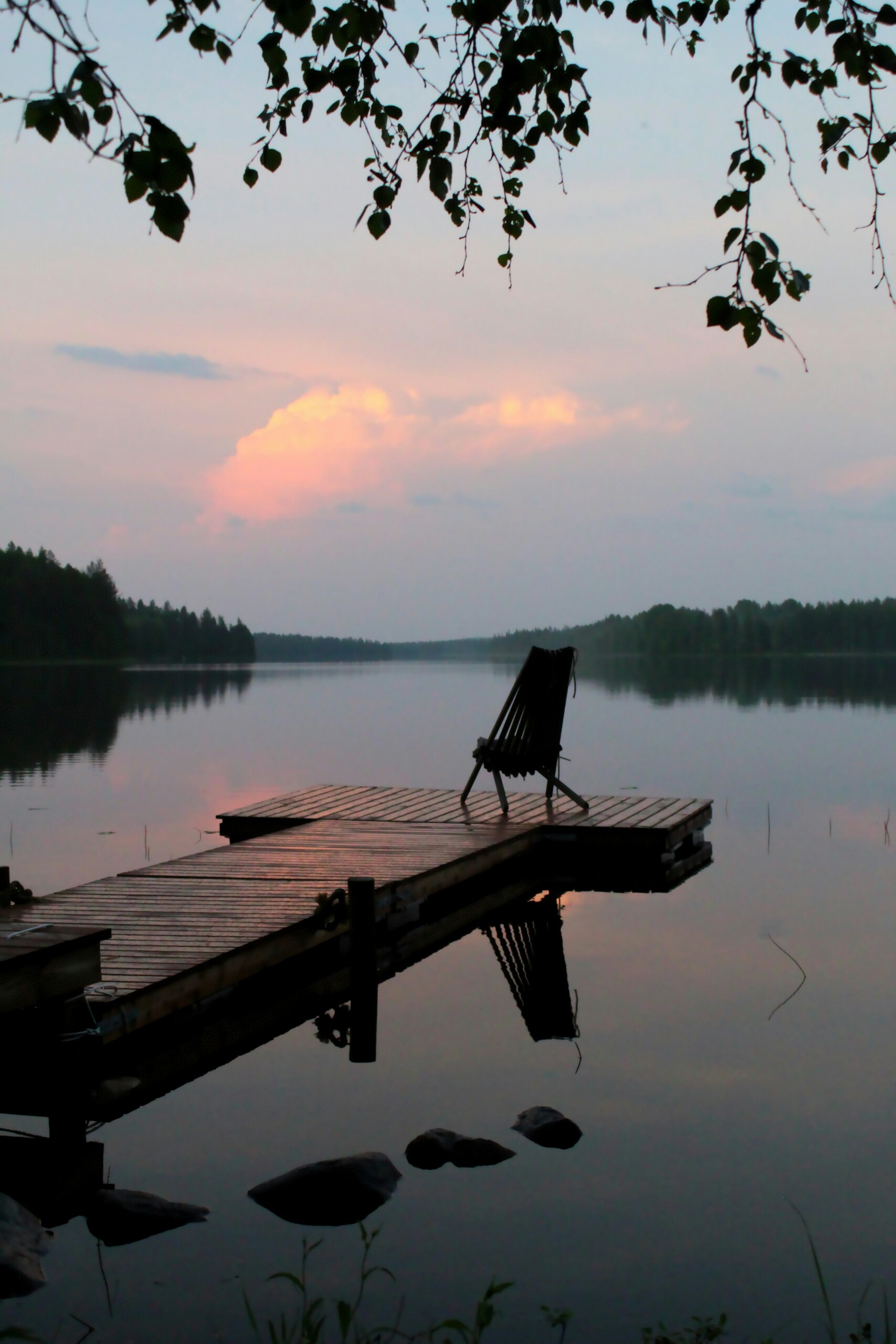 An empty chair at the end of a lake dock at dusk