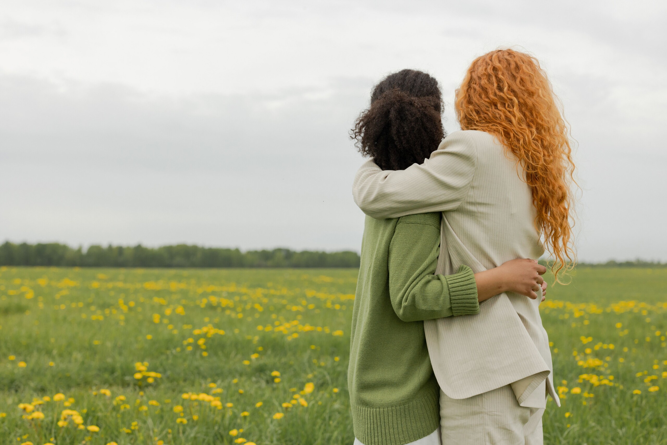 Two women embracing in a wildflower field, seen from behind