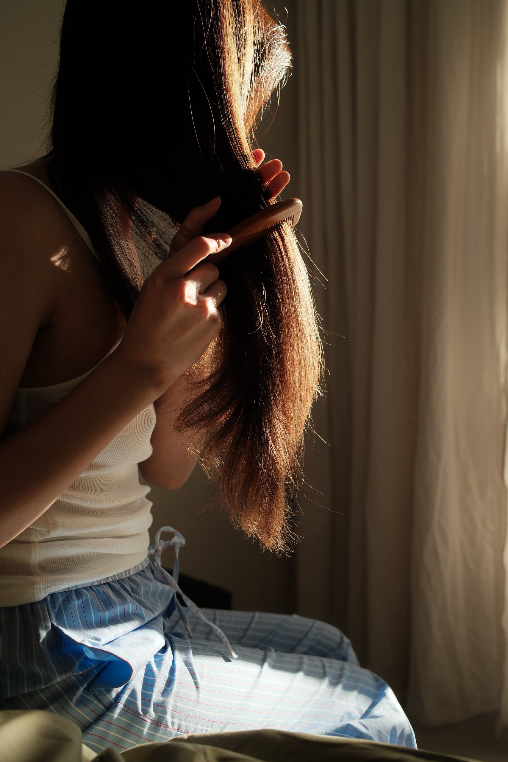 Woman combing her long hair in warm morning light, seen from behind