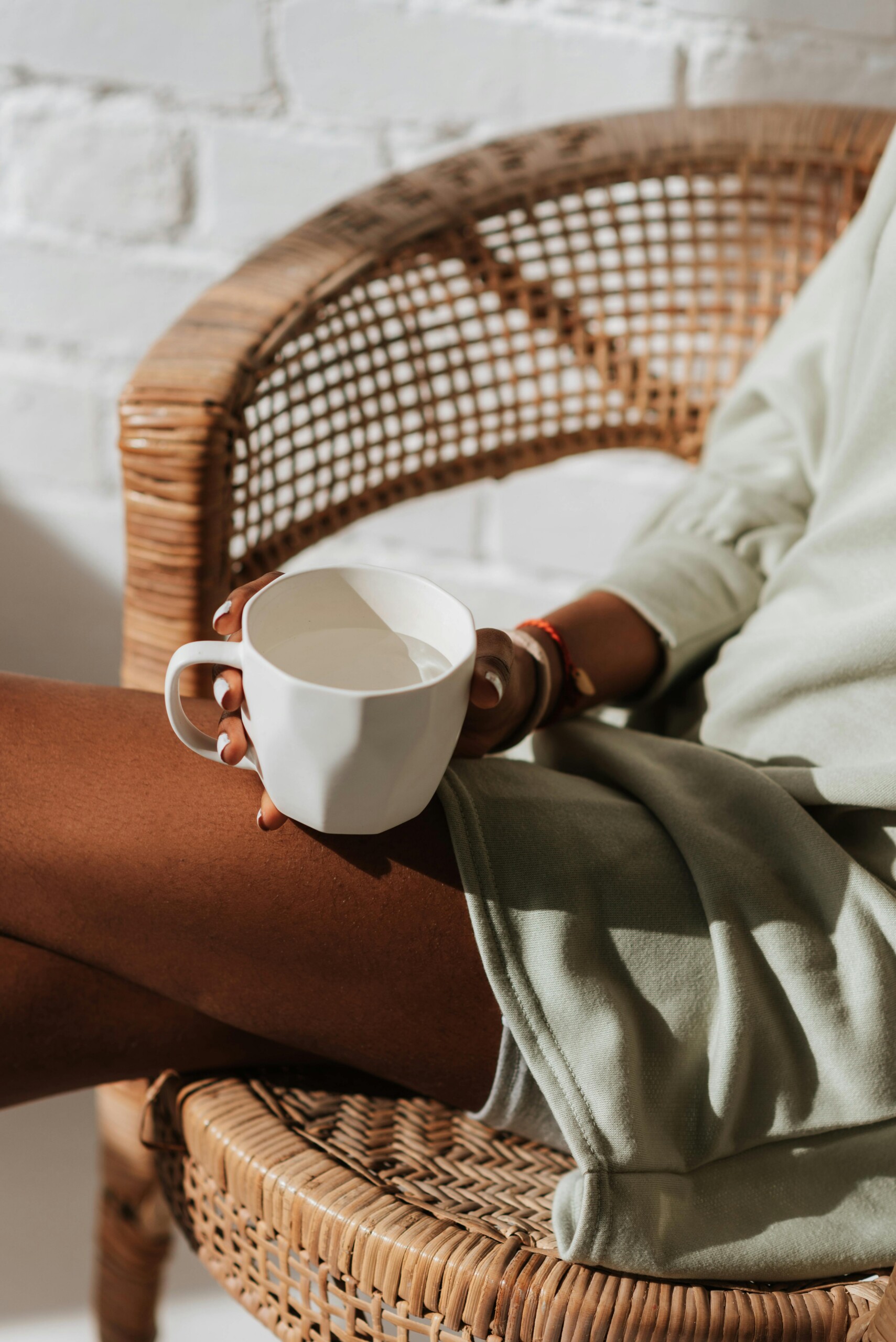 Someone sitting in a wicker chair holding a cup of tea in morning light