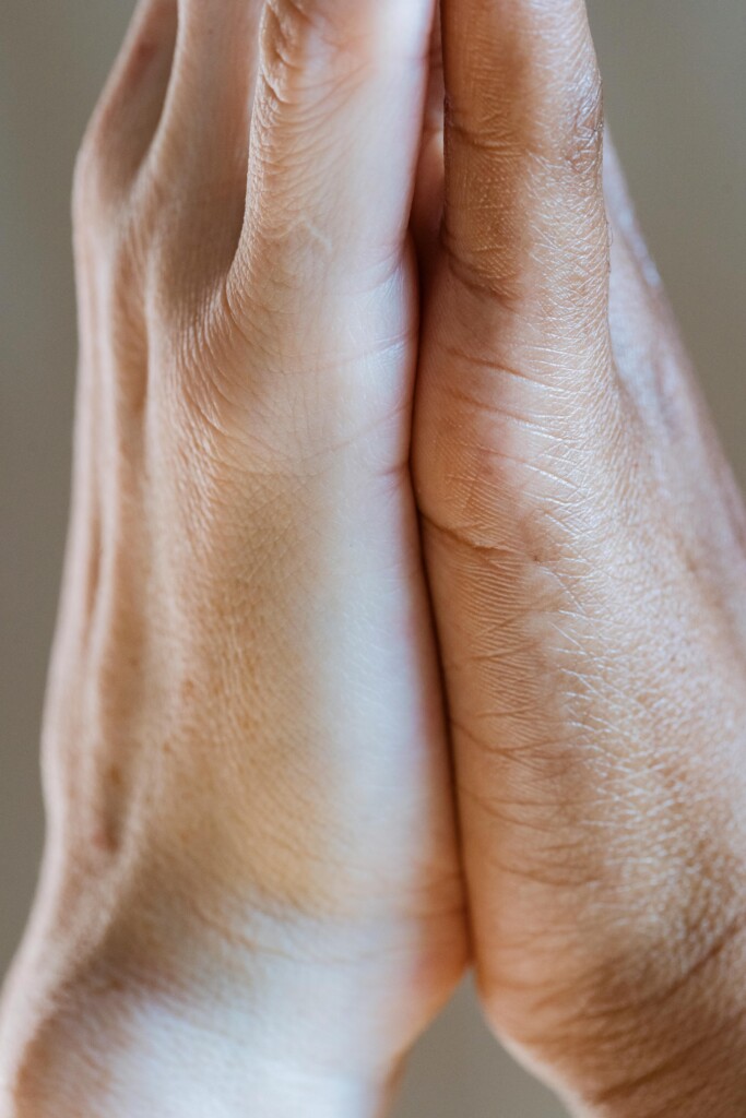 Two hands pressed gently together in soft natural light, a gesture of pause and patience