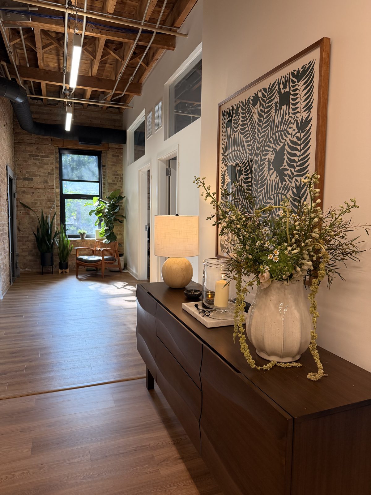 The Marra studio in River West: a console with a lamp and fresh flowers under a framed Otomi print, with the brick hallway and window beyond